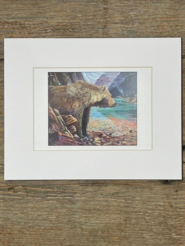 Framed artwork of a bear by a lake on a wooden surface