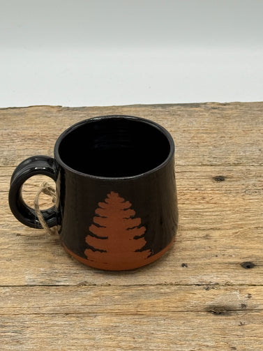 Black mug with a brown tree design on a wooden surface