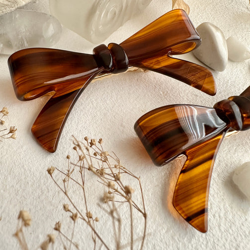 Brown bow-shaped hair clips on a textured surface with dried flowers.