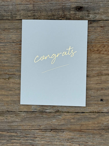 Light blue card with 'congrats' in gold on a wooden surface