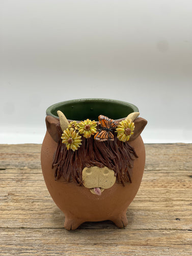 Ceramic pot shaped like a cow with floral decorations on a wooden surface
