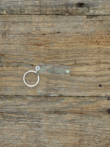 Clear keychain with text saying drive safe on a wooden surface