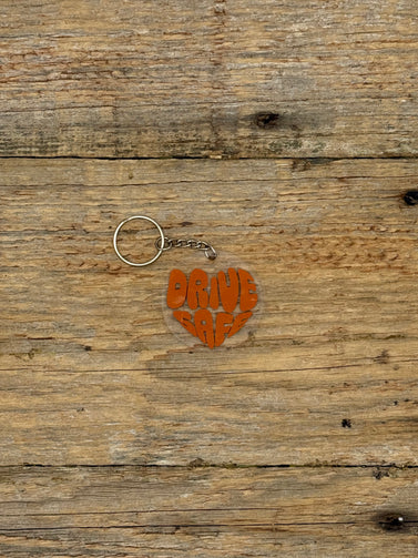 Heart-shaped keychain with 'Drive Safe' text on a wooden surface
