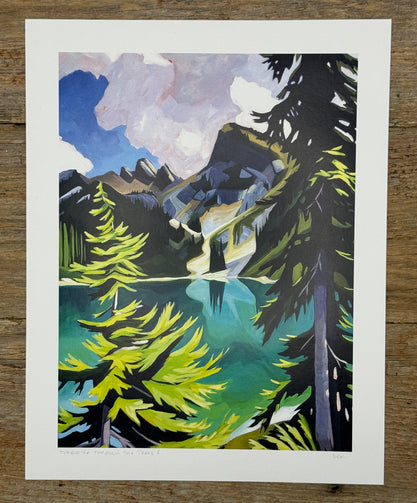 Framed artwork of a mountain landscape with trees and water on a wooden surface
