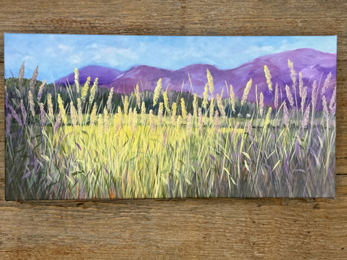 Painting of a landscape with tall grass and mountains on a wooden surface