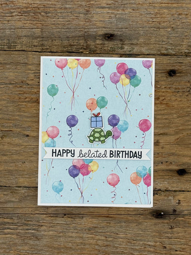 Greeting card with colorful balloons and turtle illustration on a wooden surface