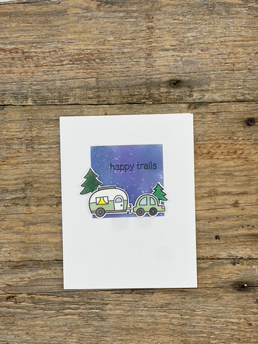 Card with a car and camper and trees on a wooden surface