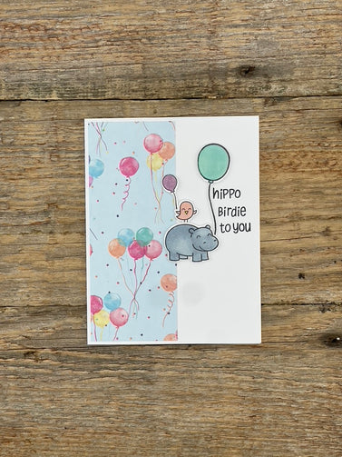 Greeting card with cartoon hippo and balloons on a wooden surface