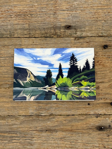 Painting of a mountain landscape with trees and a lake on a wooden surface