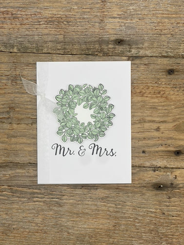 Card with green leaf wreath and 'Mr. & Mrs.' text on a wooden surface