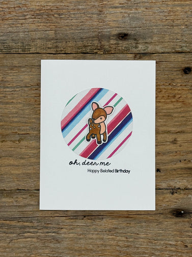 Card with a cartoon deer on a striped background, placed on a wooden surface.