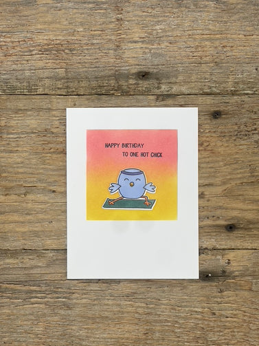 Greeting card with cartoon character and 'Happy Birthday to one hot chick' text on a wooden surface