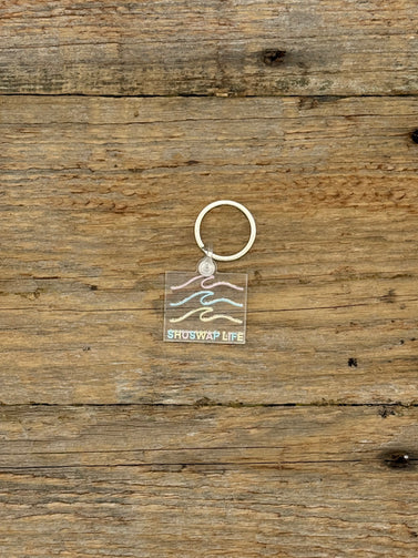 Keychain with a clear square pendant featuring wavy lines on a wooden surface