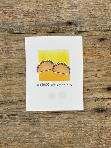 Greeting card with tacos on a yellow background, placed on a wooden surface.