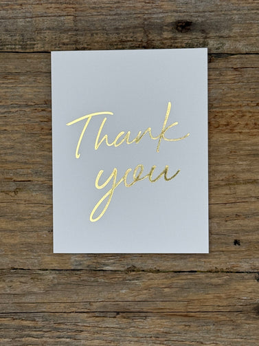 White card with 'Thank you' in gold on a wooden surface