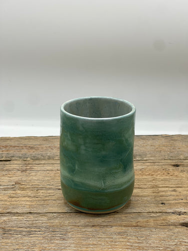 Green ceramic cup on a wooden surface with a white background