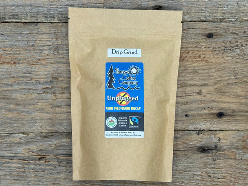 Kraft paper coffee bag with a label on a wooden surface. Unplugged Decaf by Shuswap Coffee Company