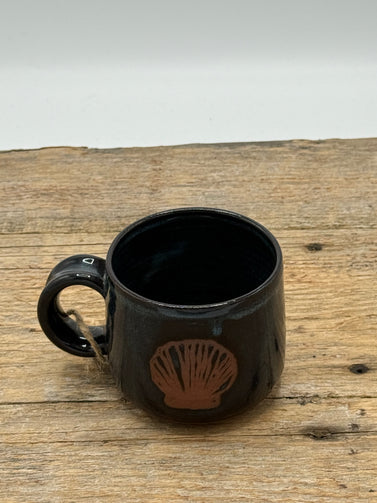 Black mug with a shell design on a wooden surface