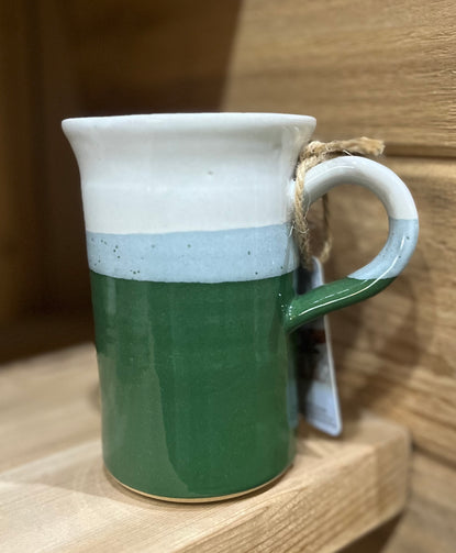 A ceramic pottery mug with a two-tone design, featuring a solid beige color at the bottom and a speckled white at the top, with a handle.