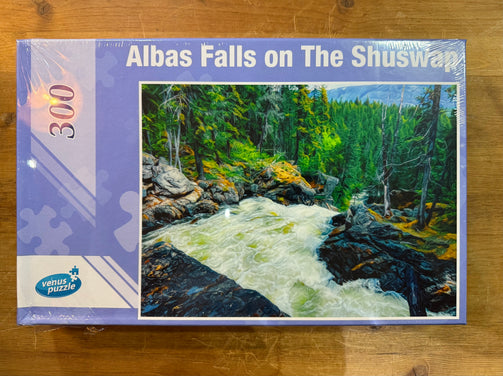 Jigsaw puzzle box featuring a scenic landscape with a waterfall and trees on a wooden surface.