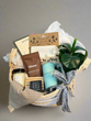 Gift basket with candles, books, and other items on a wooden floor.