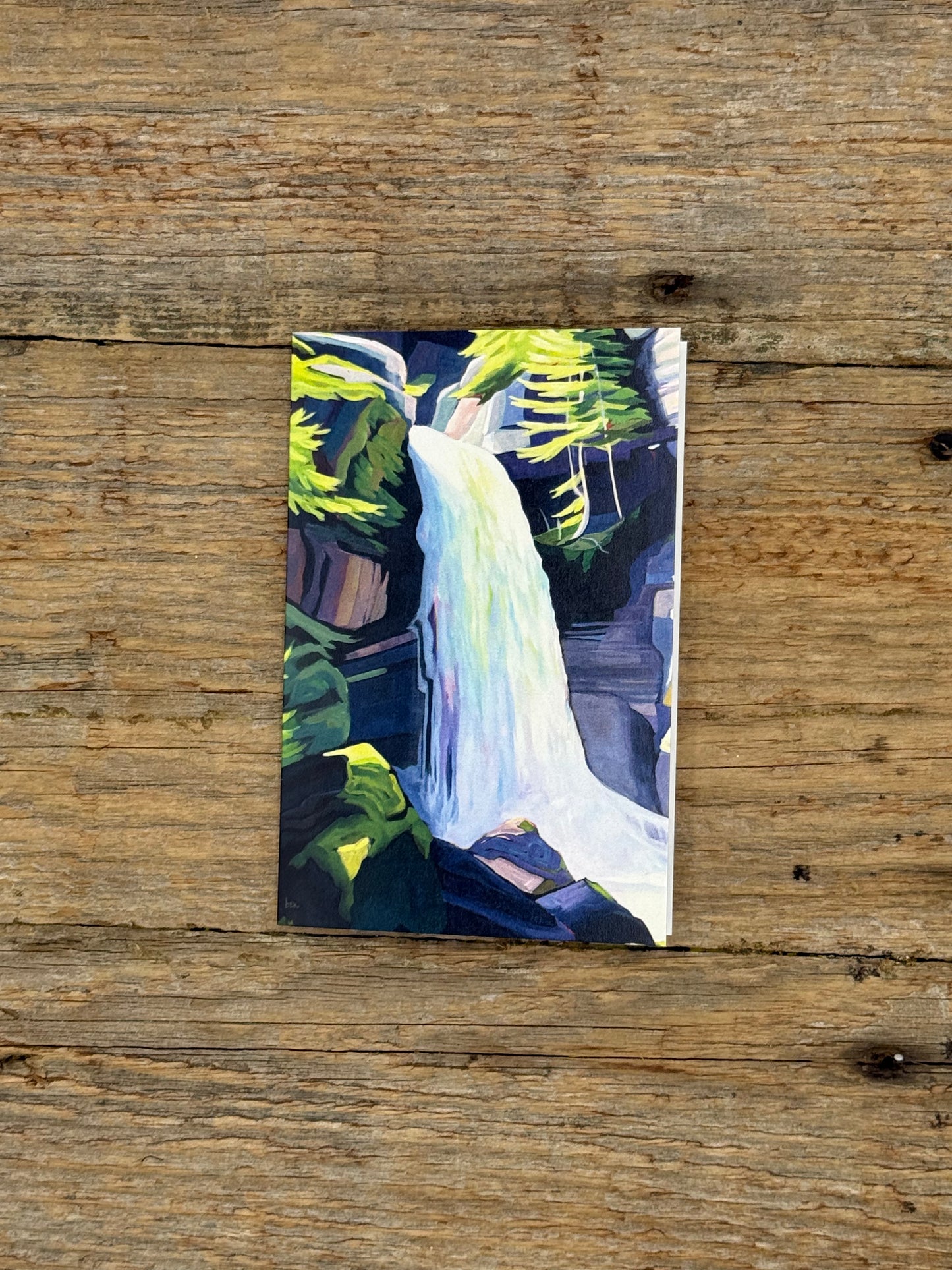 Greeting card with painting of a waterfall on a wooden surface