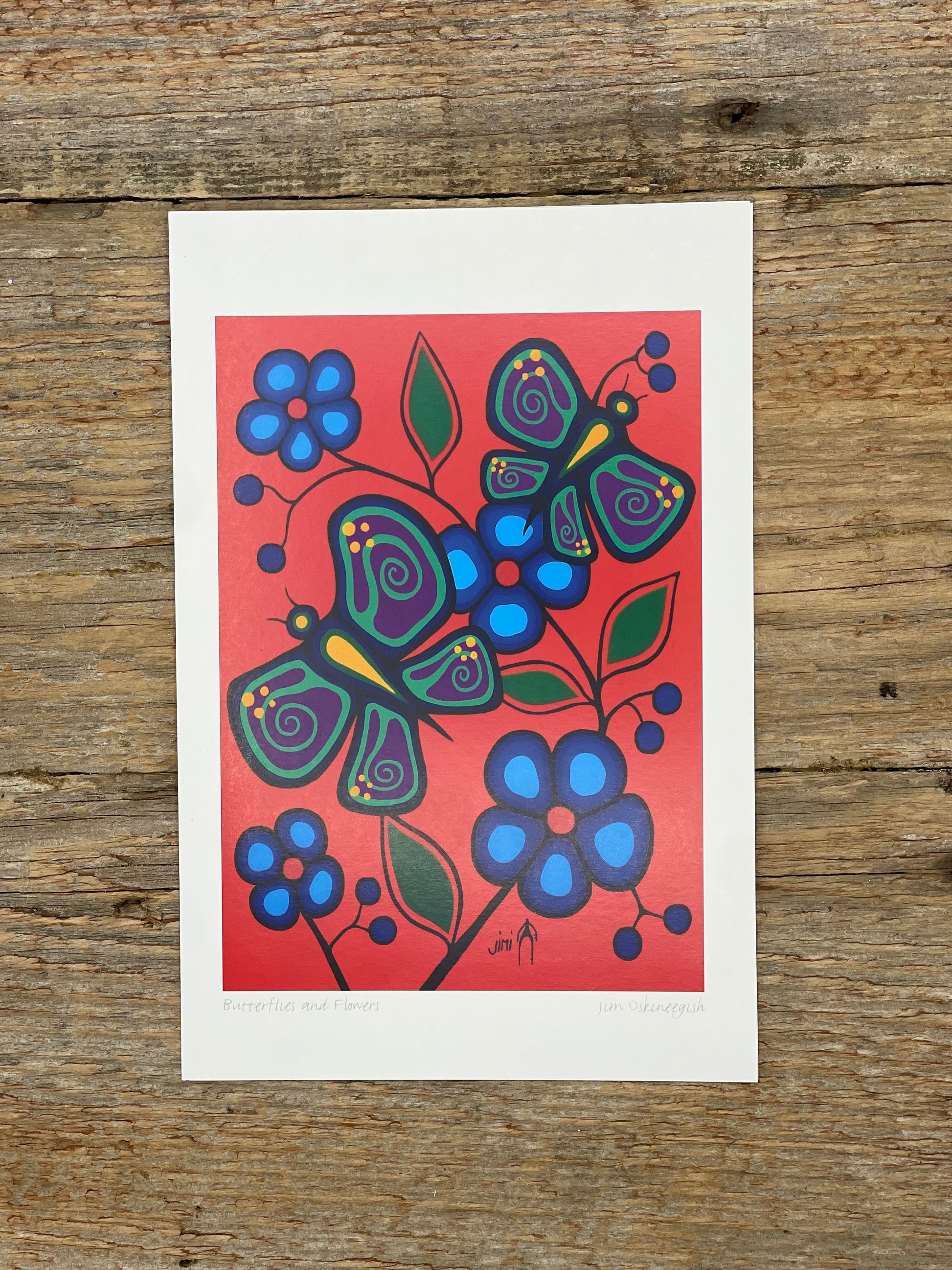 Colorful butterfly and flower illustration on a red background, placed on a wooden surface.