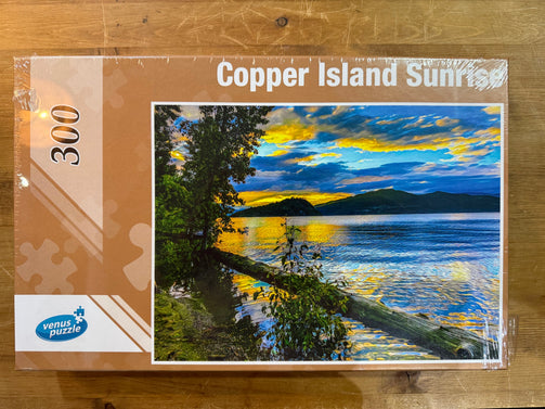 Jigsaw puzzle packaging with 'Copper Island Sunrise' design on a wooden surface