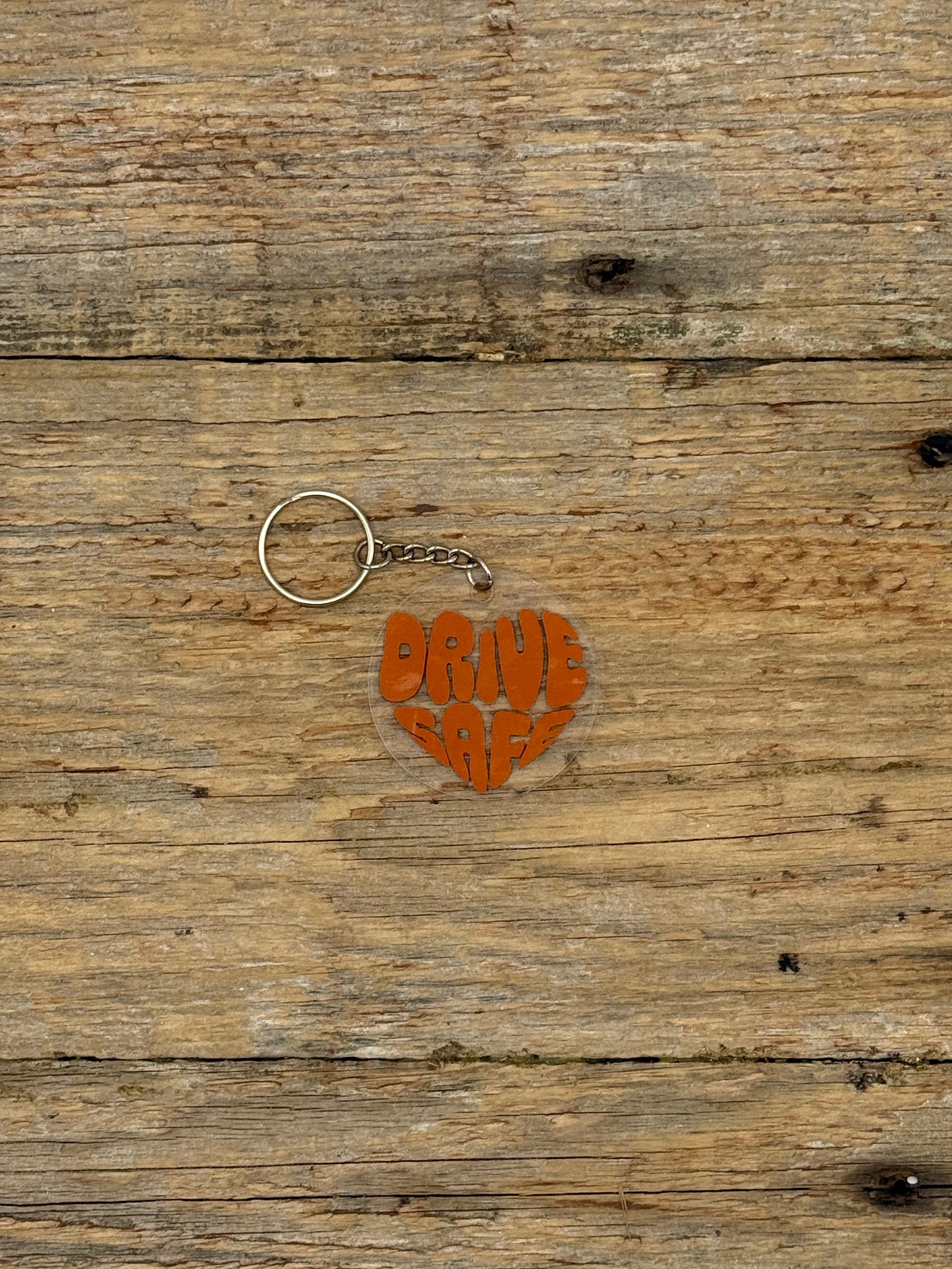 Heart-shaped keychain with 'Drive Safe' text on a wooden surface