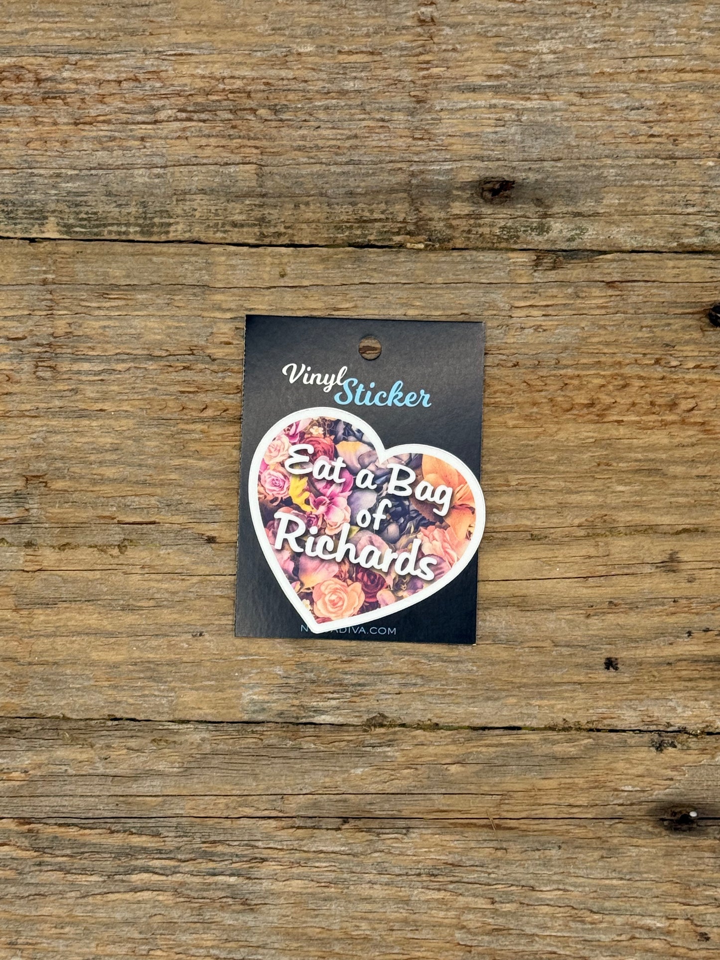 Heart-shaped vinyl sticker with floral design and text on a wooden surface