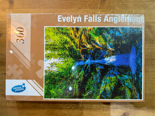Jigsaw puzzle box featuring a scenic view of Evelyn Falls Anglemont on a wooden surface.