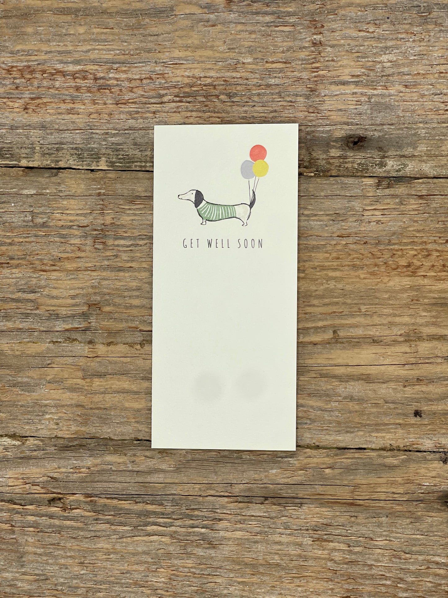 Note card with a dachshund illustration and 'Get well soon' text on a wooden surface