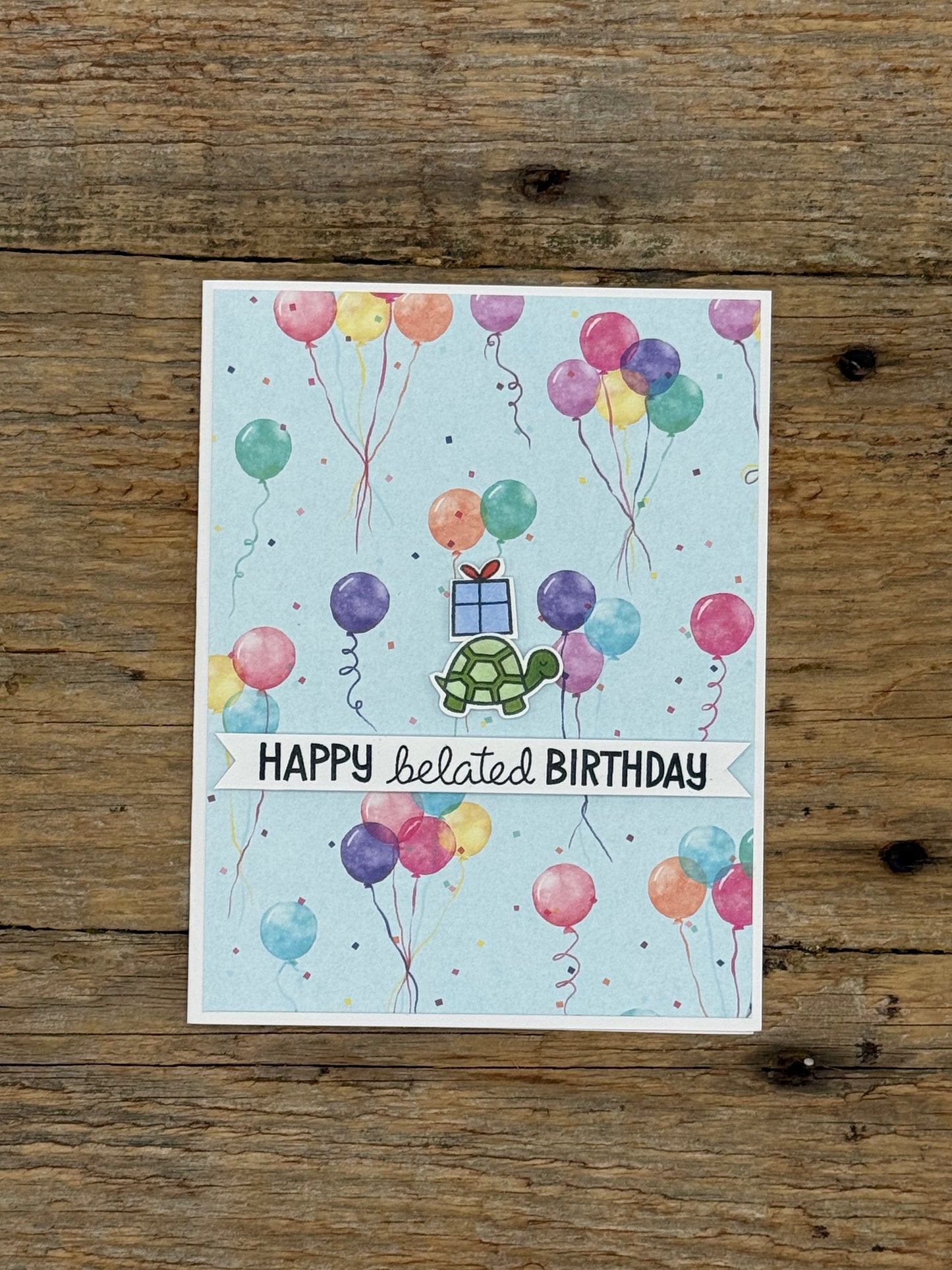 Greeting card with colorful balloons and turtle illustration on a wooden surface