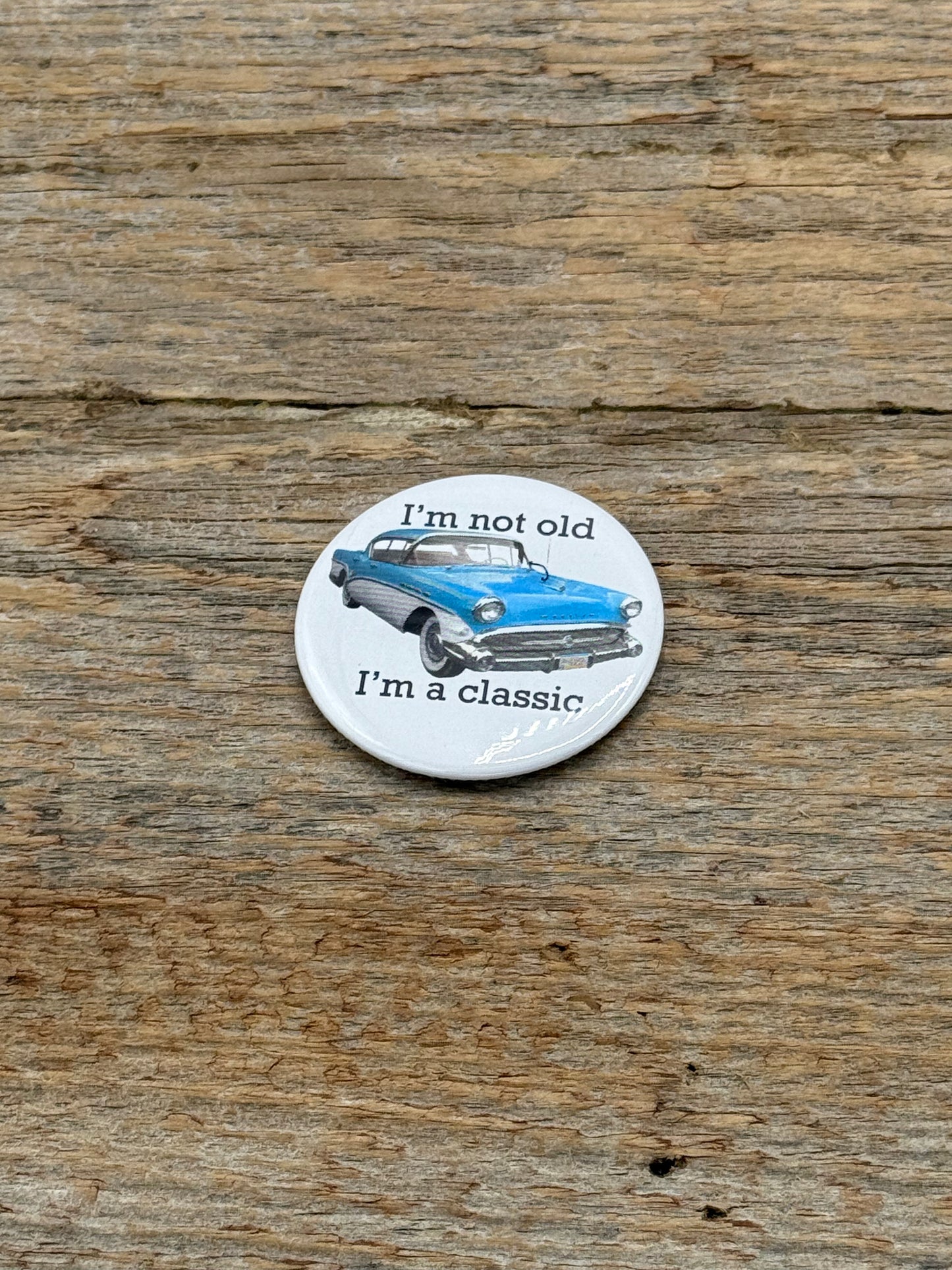 Button with vintage car illustration and text on a wooden surface
