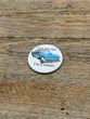 Button with vintage car illustration and text on a wooden surface