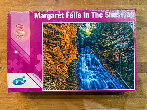 Jigsaw puzzle box featuring a waterfall with 'Margaret Falls in The Shuswap' text on a wooden surface.