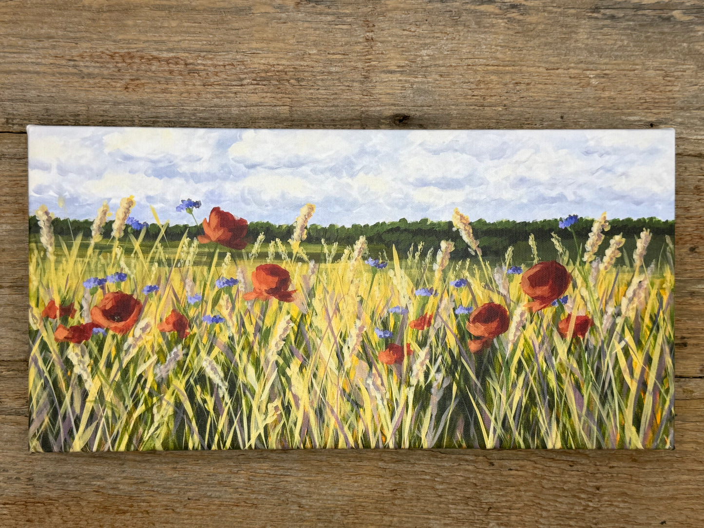 Painting of a field with red poppies and blue flowers on a wooden surface