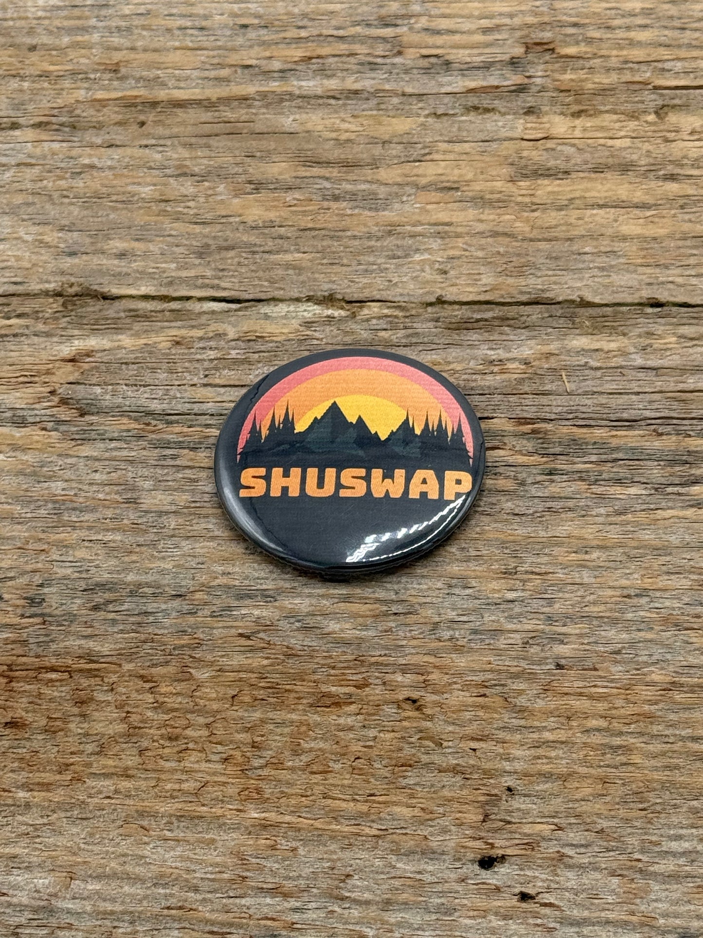 Button badge with 'SHUSWAP' text and mountain design on a wooden surface