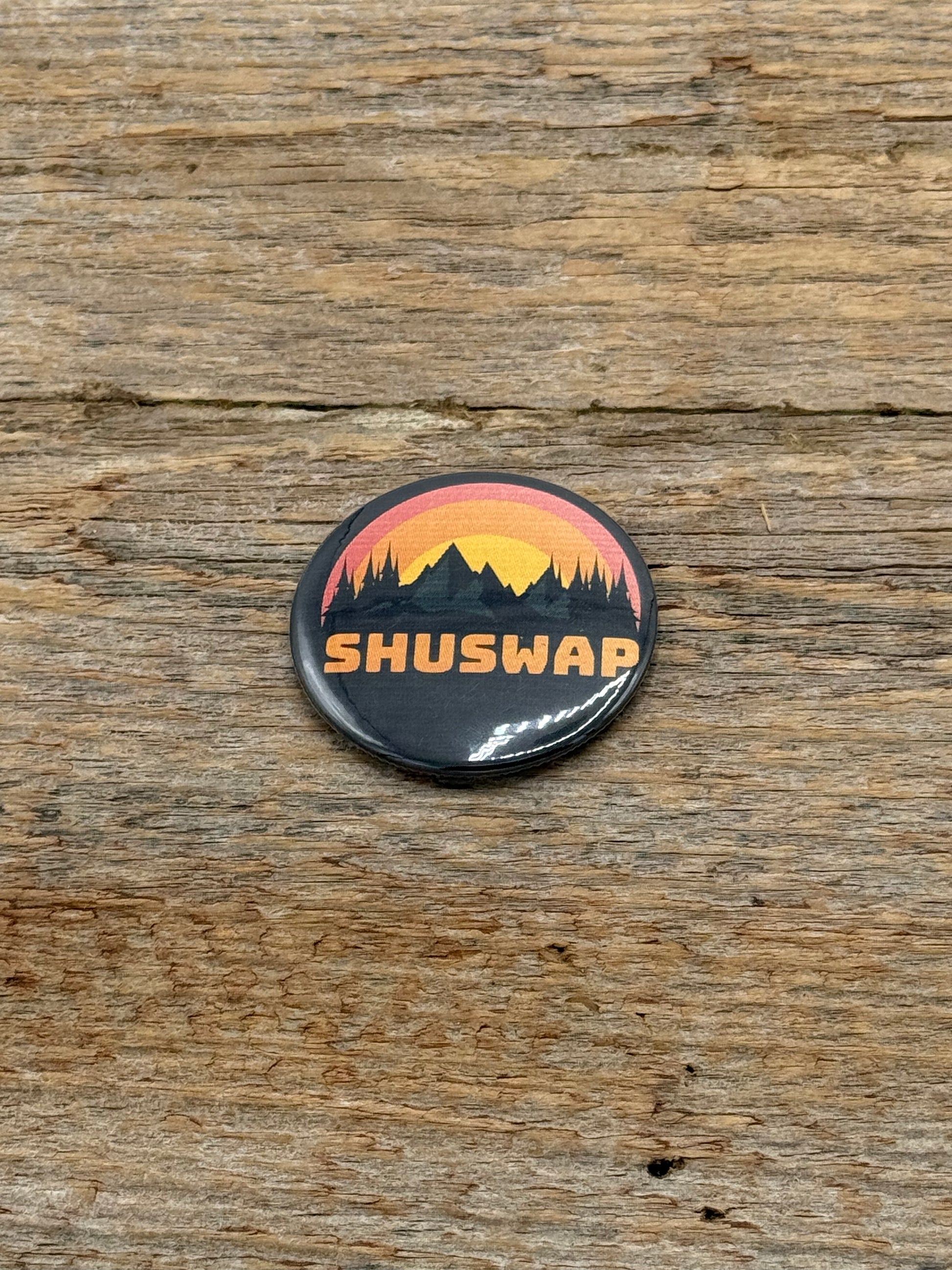Button badge with 'SHUSWAP' text and mountain design on a wooden surface