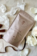 Handcrafted soap bar with a brand logo on a light background with flowers and chocolate pieces.