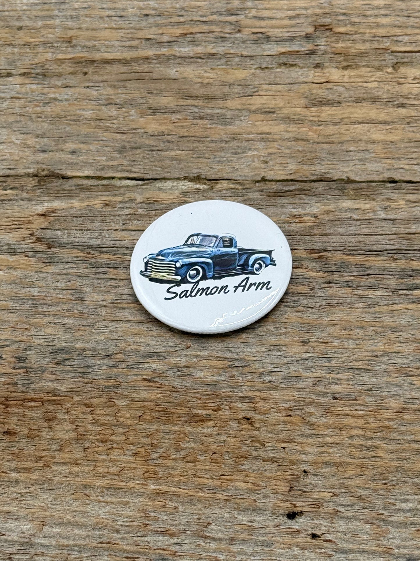 Round white magnet with vintage truck design and 'Salmon Arm' text on a wooden surface