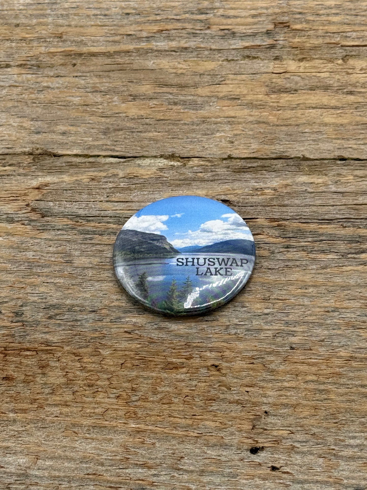 Round button with Shuswap Lake design on a wooden surface