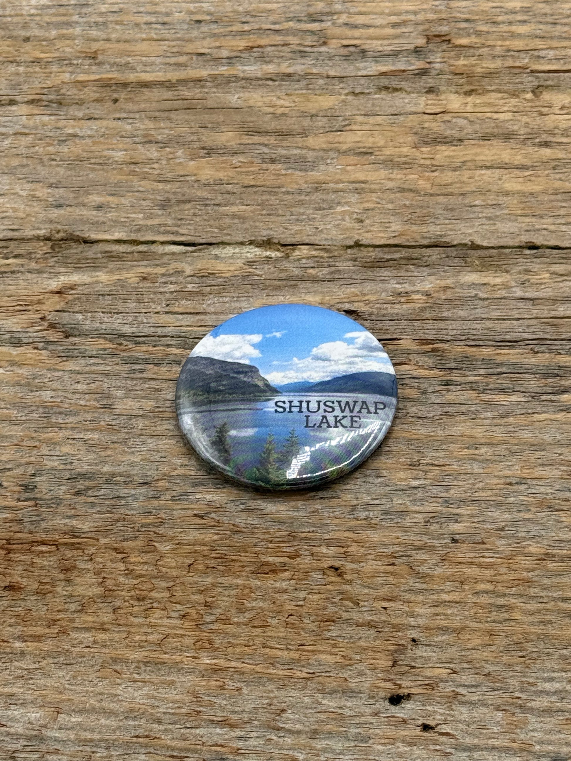 Round button with Shuswap Lake design on a wooden surface