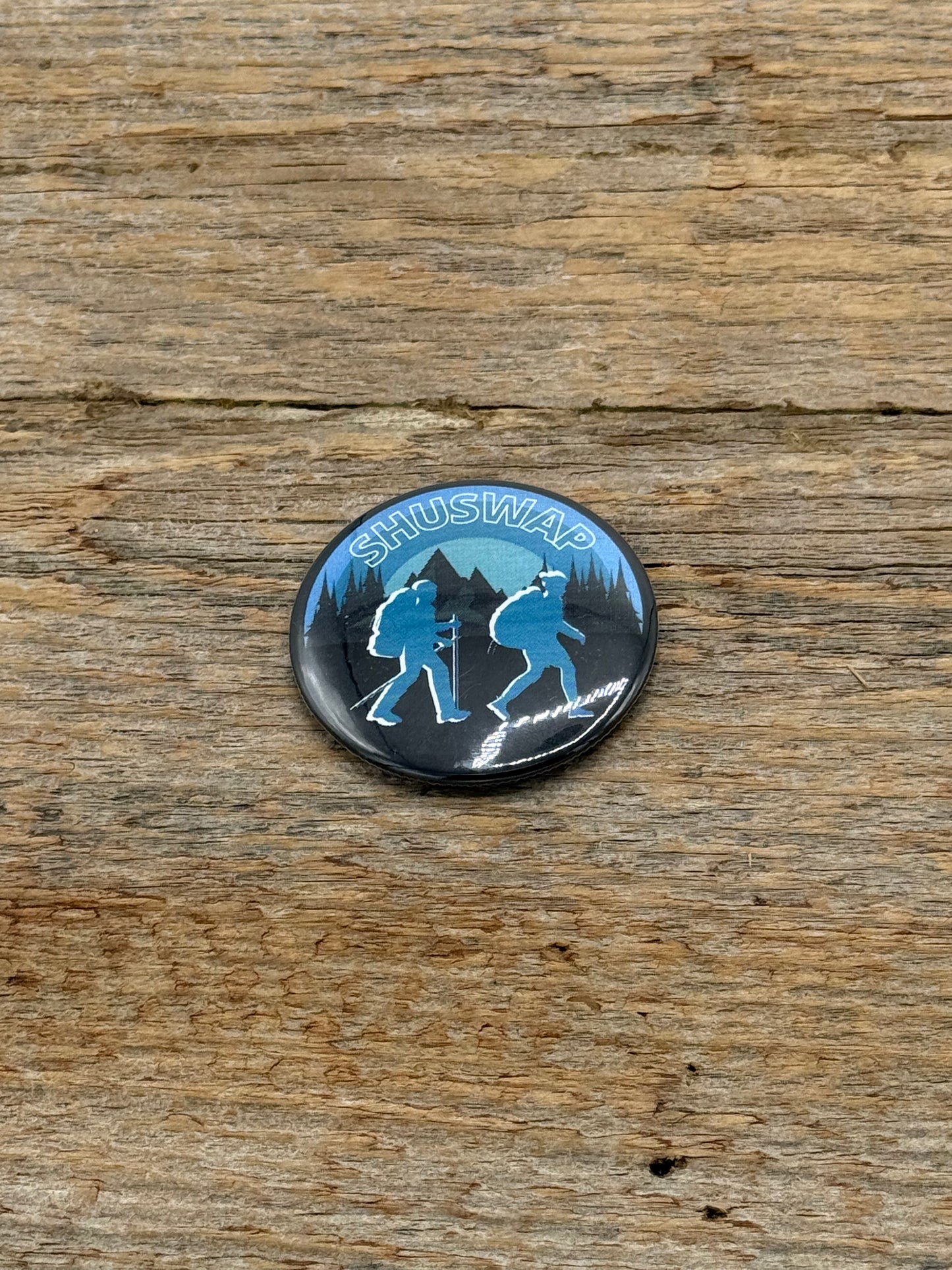Button badge with 'Shuswap' text and mountain silhouette on a wooden surface
