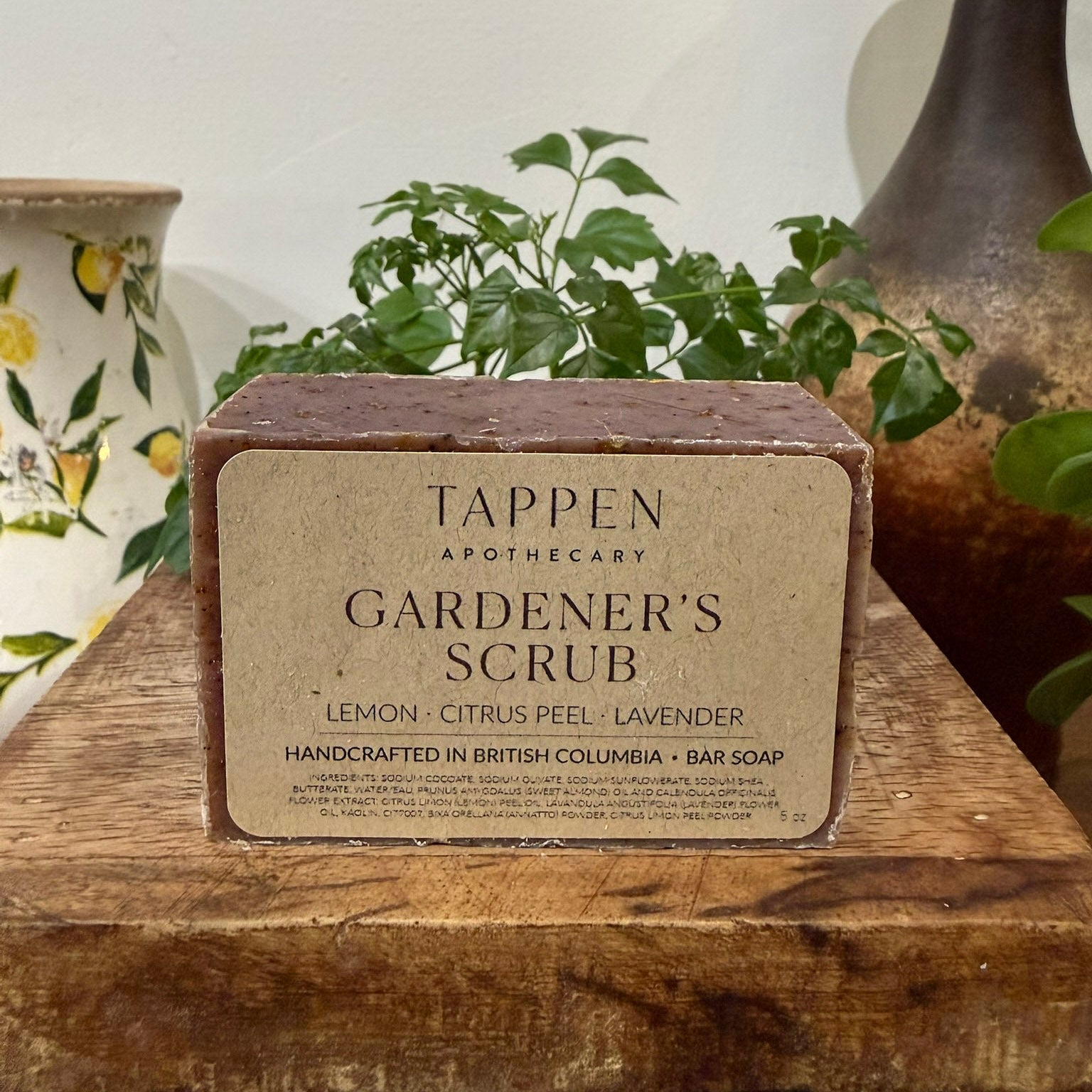 Bar of Tappen Apothecary Gardener's Scrub on a wooden surface with plants in the background