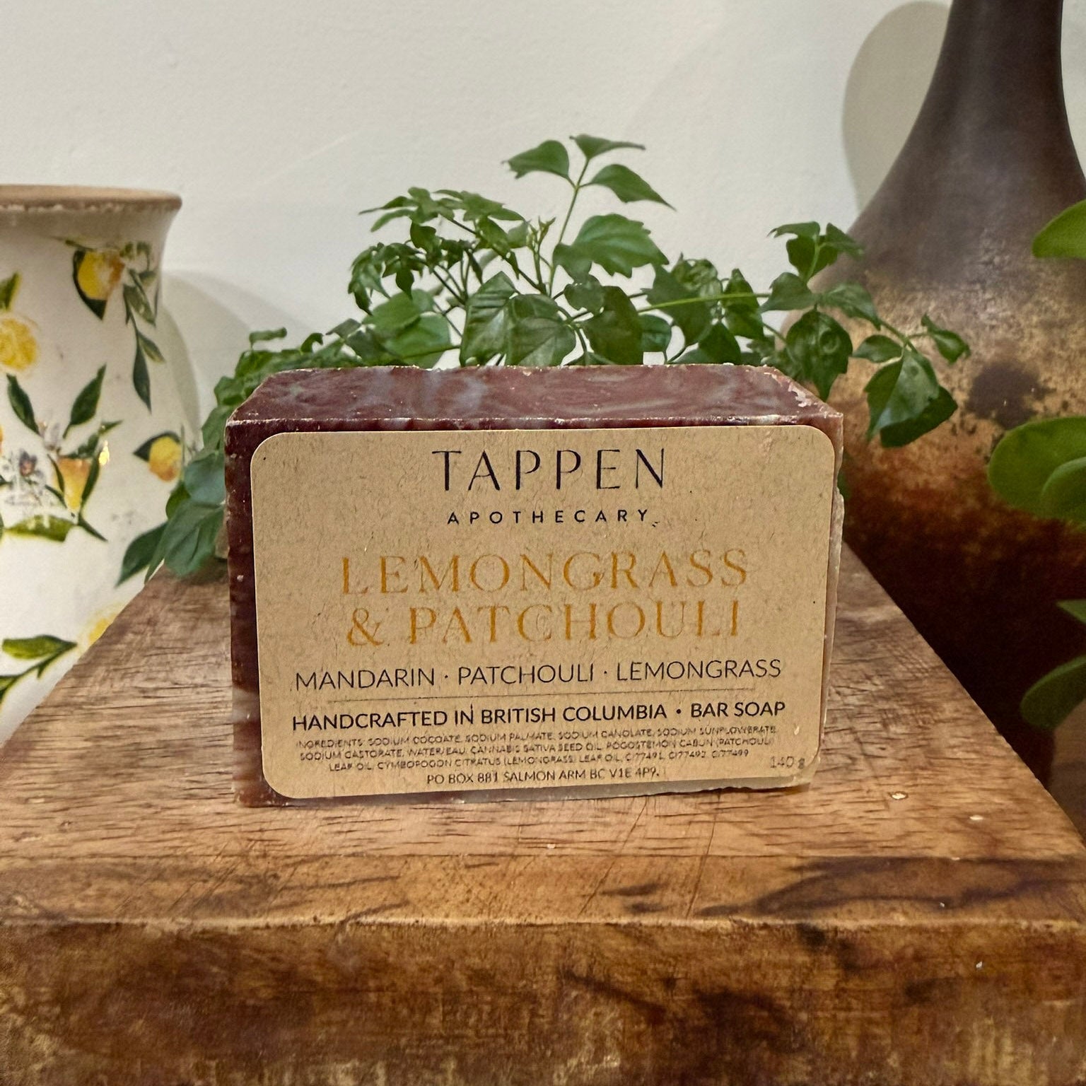 Bar of Tappen Apothecary Lemongrass & Patchouli soap on a wooden surface with plants in the background.