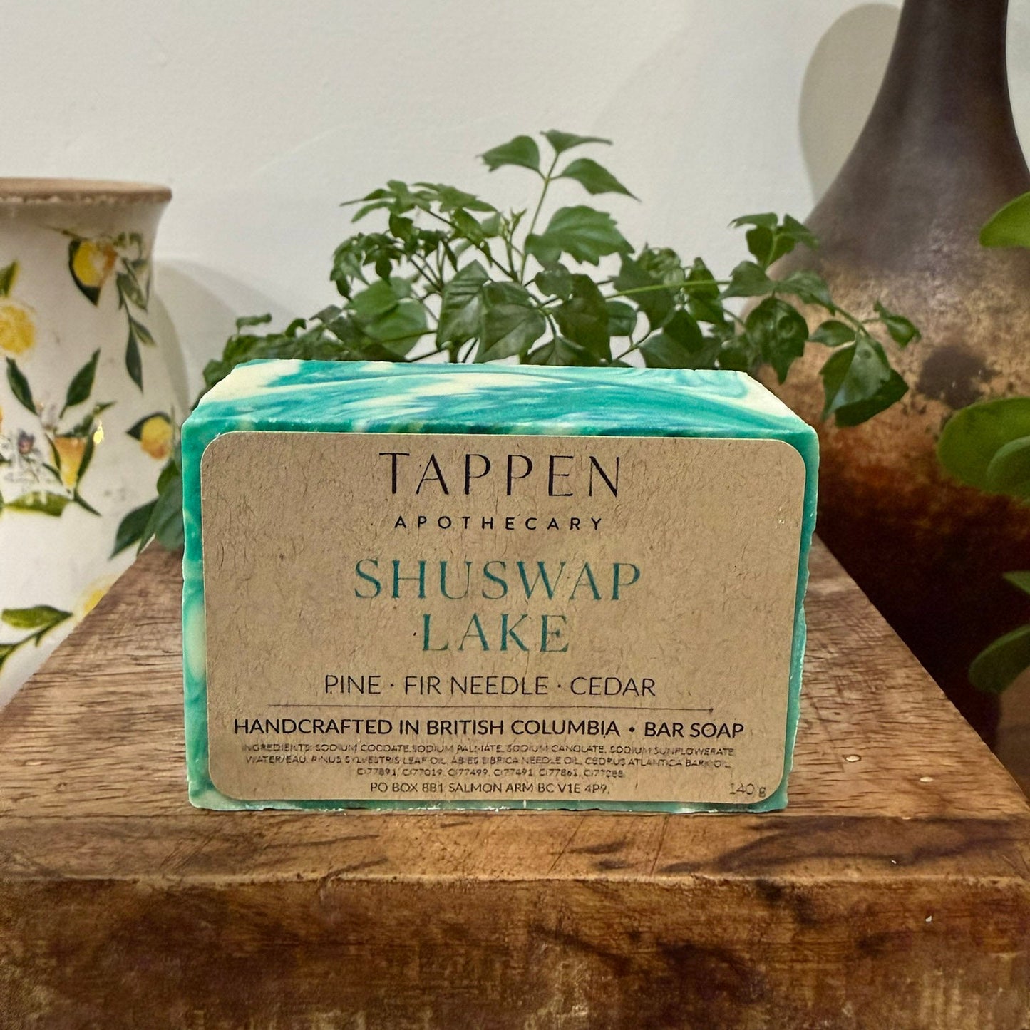 Bar of soap with Tappen Apothecary label on a wooden surface with plants in the background