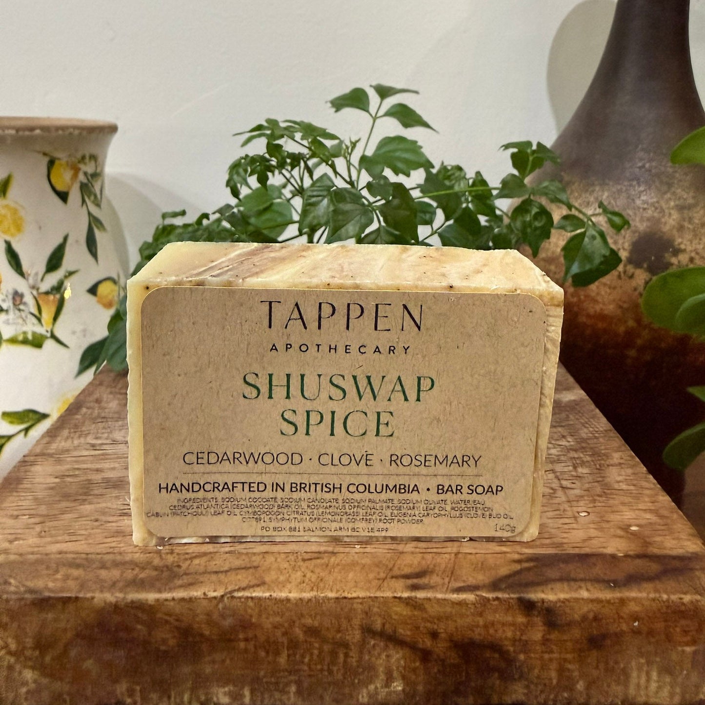 Bar of soap with 'Tappen Apothecary' branding on a wooden surface with plants in the background.