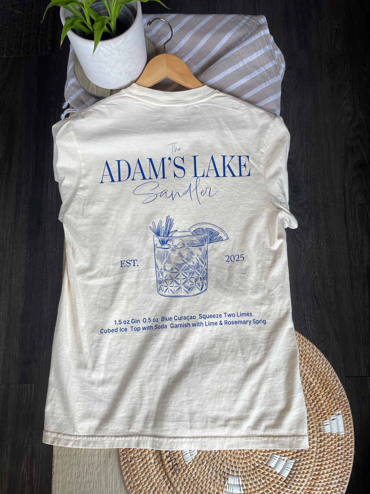 off white t-shirt with blue graphics of a rocks glass with a drink and writing that describes the drinks recipe.