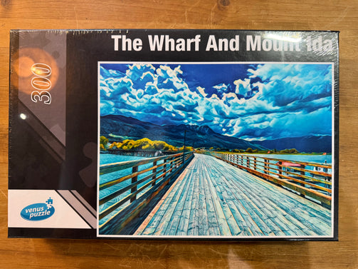 Venus Puzzle packaging of 'The Wharf And Mount Ida' with a scenic illustration on a wooden surface.